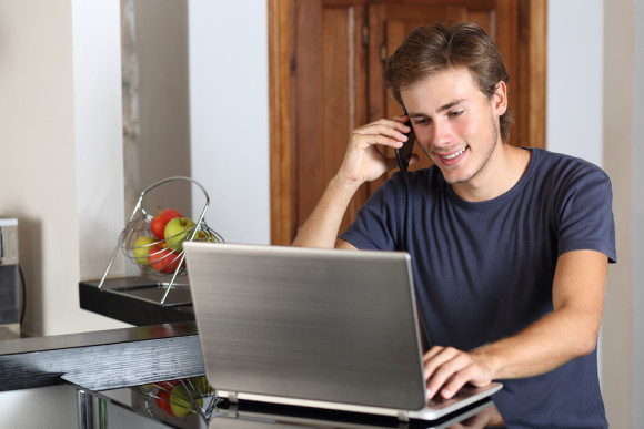 Entrepreneur man on the phone working with a laptop in the kitchen at home
