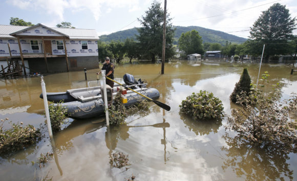 Lt. Dennis Feazell, of the West Virginia Department of Natural Resources, keeps his boat on station as he and a co-worker search flooded homes in Rainelle, W. Va., Saturday, June 25, 2016. Heavy rains that pummeled West Virginia left multiple people dead, and authorities said Saturday that an unknown number of people in the hardest-hit county remained unaccounted for. (AP Photo/Steve Helber)