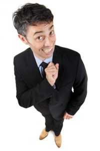 Obsequious businessman with a toothy beaming sycophantic smile standing looking perky and wide eyed looking up at the camera, high angle fun portrait isolated on white