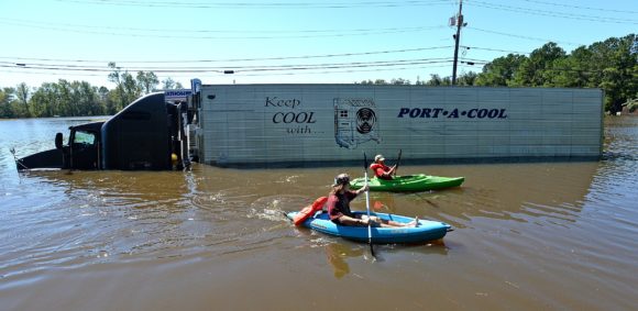 Anthony Writebol, left, and his cousin, Melissa Hill paddle past a stranded tractor trailer on Hwy 211 in Lumberton, N.C., Sunday, Oct. 9, 2016. They were heading to meet friends who were going to let them stay after their neighborhood "wayfarer" was flooded overnight by heavy rains associated with Hurricane Matthew. (Chuck Liddy/The Charlotte Observer via AP)