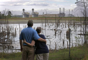 In this April 25, 2014, file photo, Bryant Gobble, left, embraces his wife, Sherry Gobble, right, as they look from their yard across an ash pond full of dead trees toward Duke Energy's Buck Steam Station in Dukeville, N.C. North Carolina officials are advising dozens of residents near Duke Energy coal ash sumps not to drink or cook with water from their wells after tests showed contamination with toxic heavy metals. (AP Photo/Chuck Burton, File)