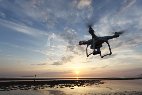 Remote controlled drone Dji Phantom 3 equipped with high resolution video camera flying above the beach against a sunset.