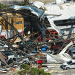 Hurricane Ian destroyed industrial building with damaged cars under ruins in Florida. Natural disaster and its consequences.