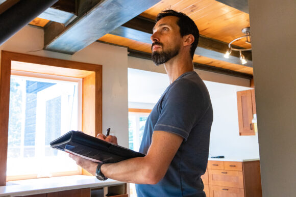 A close up and side view of a tall caucasian male with short black hair and beard, inspecting a home during an indoor environmental quality assessment.