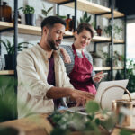 Man and woman shop assistants with laptop working in indoor potted plant store, small business concept.