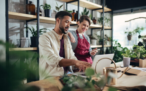 Man and woman shop assistants with laptop working in indoor potted plant store, small business concept.