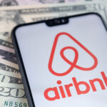 Stafford / United Kingdom - November 15 2020: Airbnb app logo seen on the screen of smartphone, placed on dollar bills.