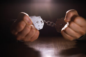 stressed out businessman hands bothered with handcuffs suffering at custody for concept of suspicious business, hostage or corporate justice, above view
