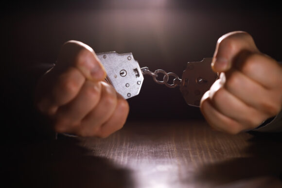 stressed out businessman hands bothered with handcuffs suffering at custody for concept of suspicious business, hostage or corporate justice, above view