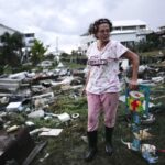 FILE - Jewell Baggett stands beside a Christmas decoration she recovered from the wreckage of her mother's home, as she searches for anything salvageable from the trailer home her grandfather had acquired in 1973 and built multiple additions on to over the decades, in Horseshoe Beach, Fla., after the passage of Hurricane Idalia, Wednesday, Aug. 30, 2023. (AP Photo/Rebecca Blackwell, File)