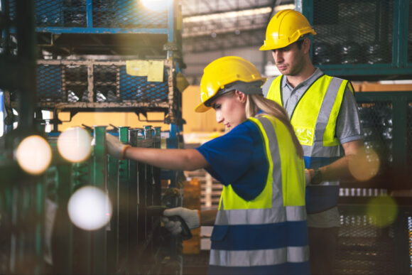 Caucasian Male and Female Warehouse Workers Wearing Safety Hardhat and Safety Jacket Working Together in Factory, Factory Workers Checking and Quality Control Product in Storage Warehouse.