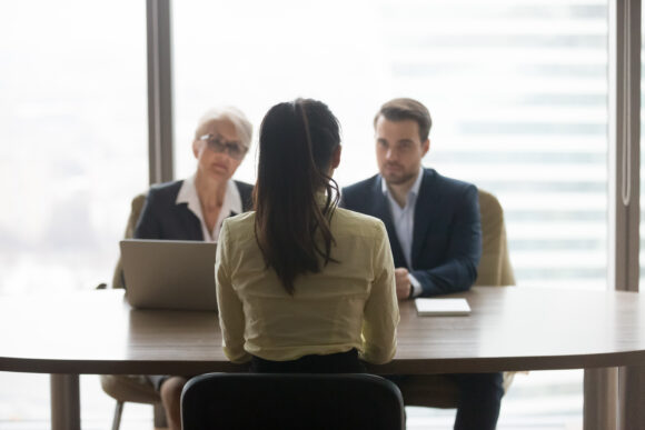 Rear view of female job applicant talking to recruiters listen at job interview, woman vacancy candidate seeker sits back making first impression on hr managers in office, hiring recruitment concept