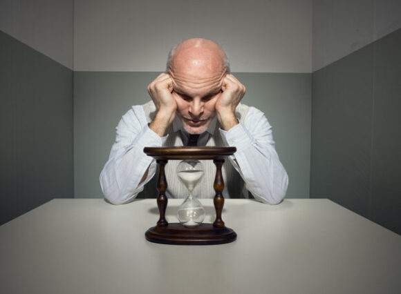 Bored vintage businessman waiting at desk with hourglass.