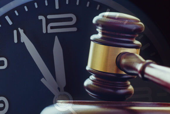 Wood and brass gavel standing upright on its base with a clock dial showing five to twelve behind in a law enforcement or auction concept