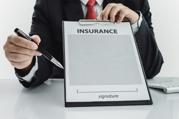 young man in suit in his office showing an insurance policy and pointing with a pen where the policyholder must to sign