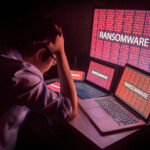 Young Asian male frustrated, confused and headache by ransomware attack on desktop screen, notebook and smartphone, cyber attack and internet security concepts