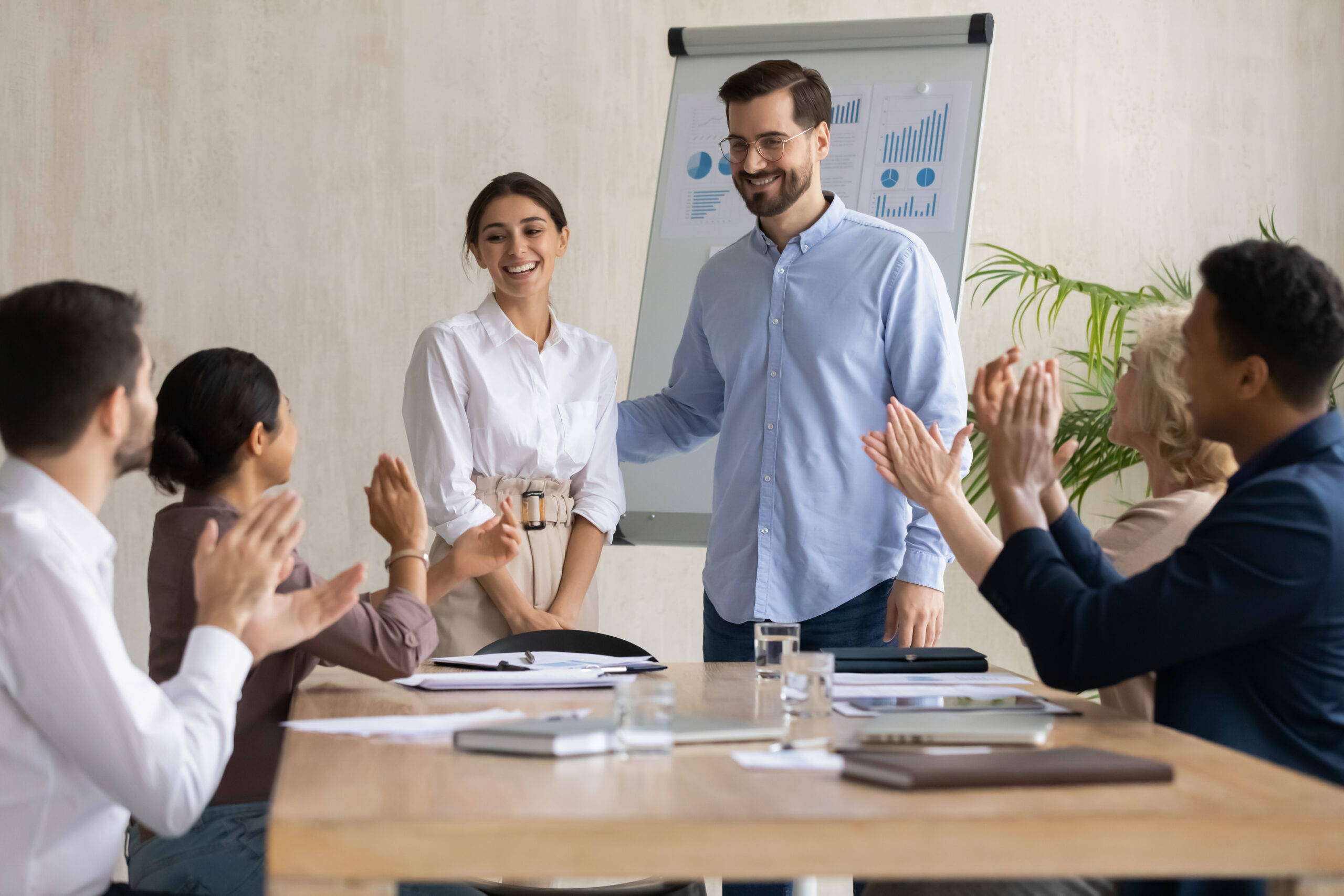 Smiling male leader praising happy millennial arab colleague at group meeting. Smiling diverse coworkers applauding, supporting new worker or congratulating with personal professional achievement.