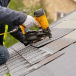 Workman using pneumatic nail gun install tile on roof of new house