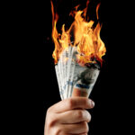 Male hand close-up, holds burning money in hands, burning US dollars. Black background, isolate. The concept of inflation, a decrease in the purchase of foreign currency, and devolution.