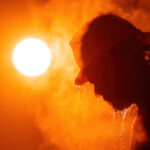 A construction worker's silhouette against a blazing sun, sweat dripping from their brow, the air around them shimmering with an intense heat haze, capturing the physical toll of extreme heat
