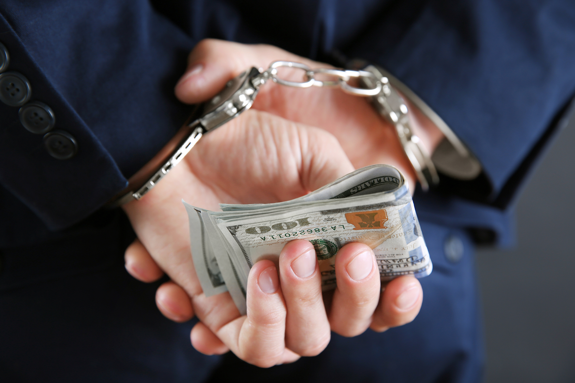 Man in handcuffs holding dollar banknotes behind the back, close up