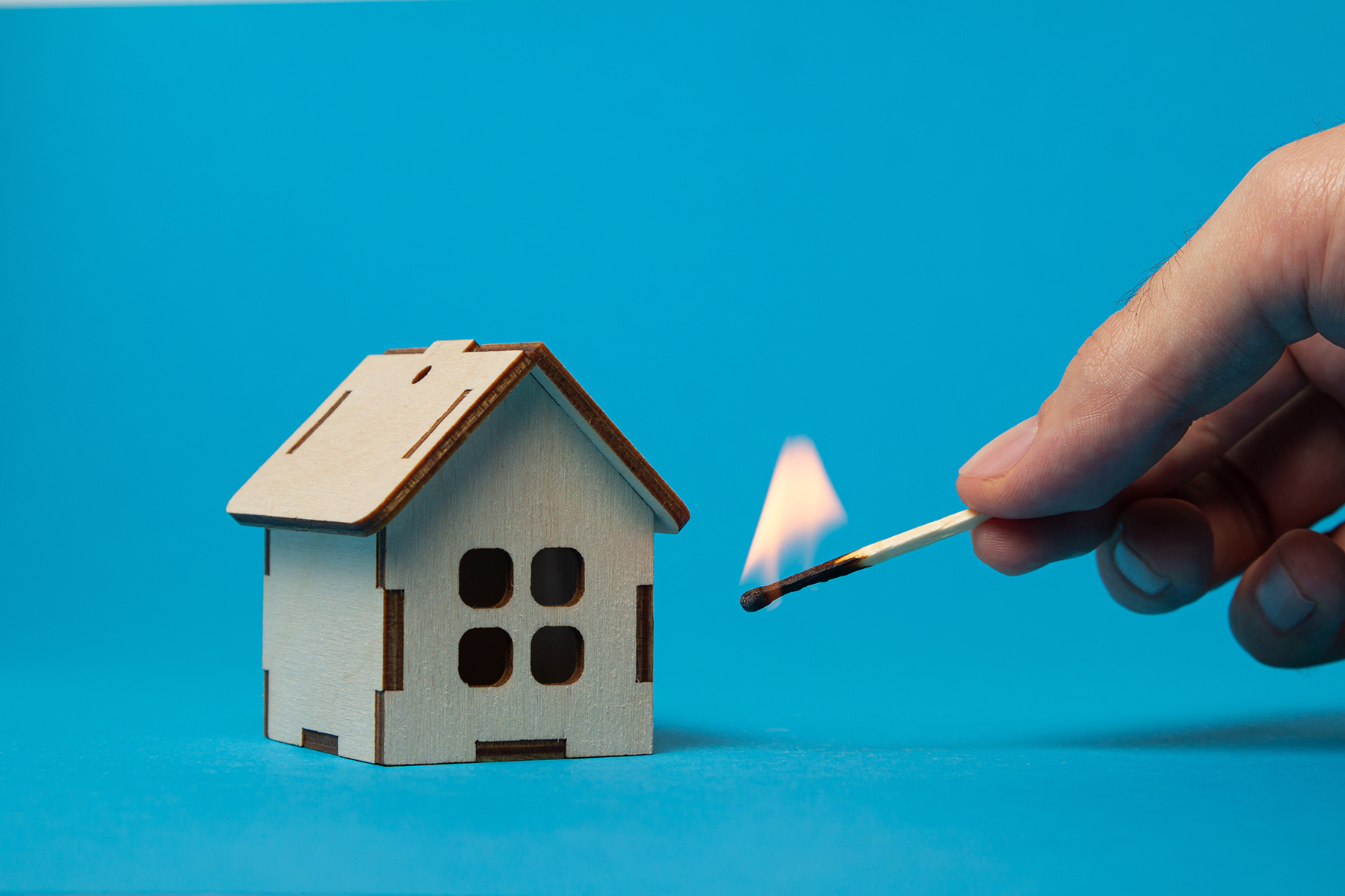 A burning match next to a wooden house on a blue background. Rea