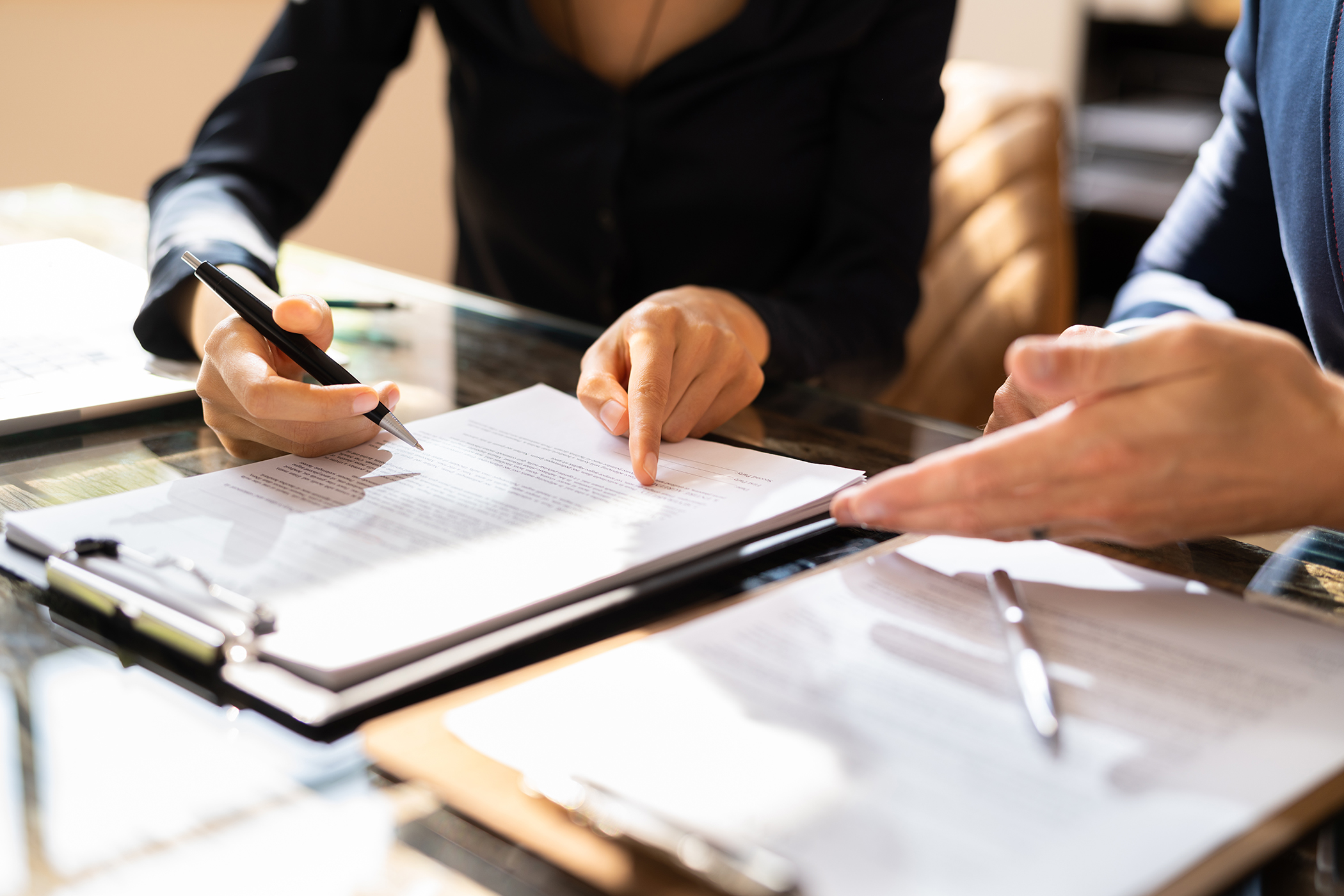 Close-up Of Two Businesspeople Hand Working On Contract Paper Over Desk