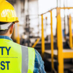 Worker in safety vest and helmet facing factory floor, highlight
