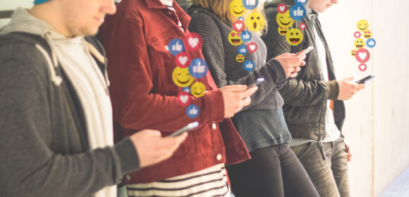 Social network concept. Like, love, wow and smile icons pop up from smartphone screen. Young people addicted to social media apps. Unrecognizable people.