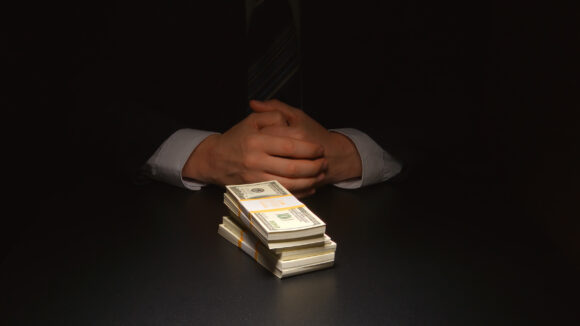 BRIBE: Businessman sits near a heap money on a table