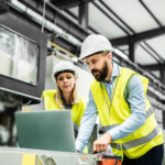 A portrait of a mature industrial man and woman engineer with laptop in a factory, working.