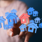 Person's hand touching a 3D model of a house or home. Property concept