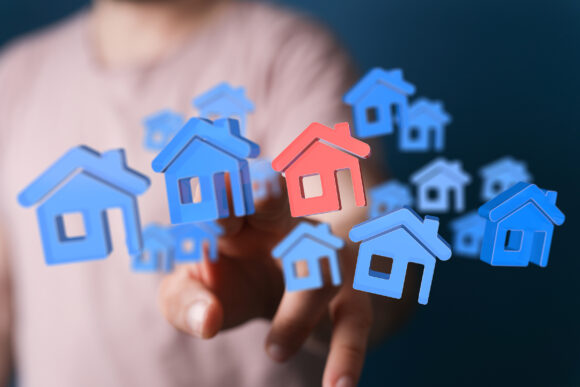 Person's hand touching a 3D model of a house or home. Property concept