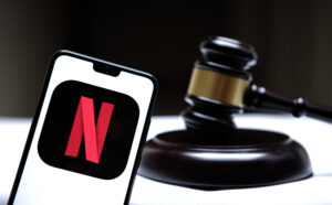 Stafford, United Kingdom - December 15 2020: Netflix logo seen on the smartphone placed next to the judges gavel. Concept for a lawsuit, legal case, antitrust and fine. Real photo, not a montage.