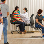 Variety ages citizens standing in a row and waiting for a vaccine injection while medical people injecting to senior women in face mask. Covid-19 or coronavirus herd immunity concept.