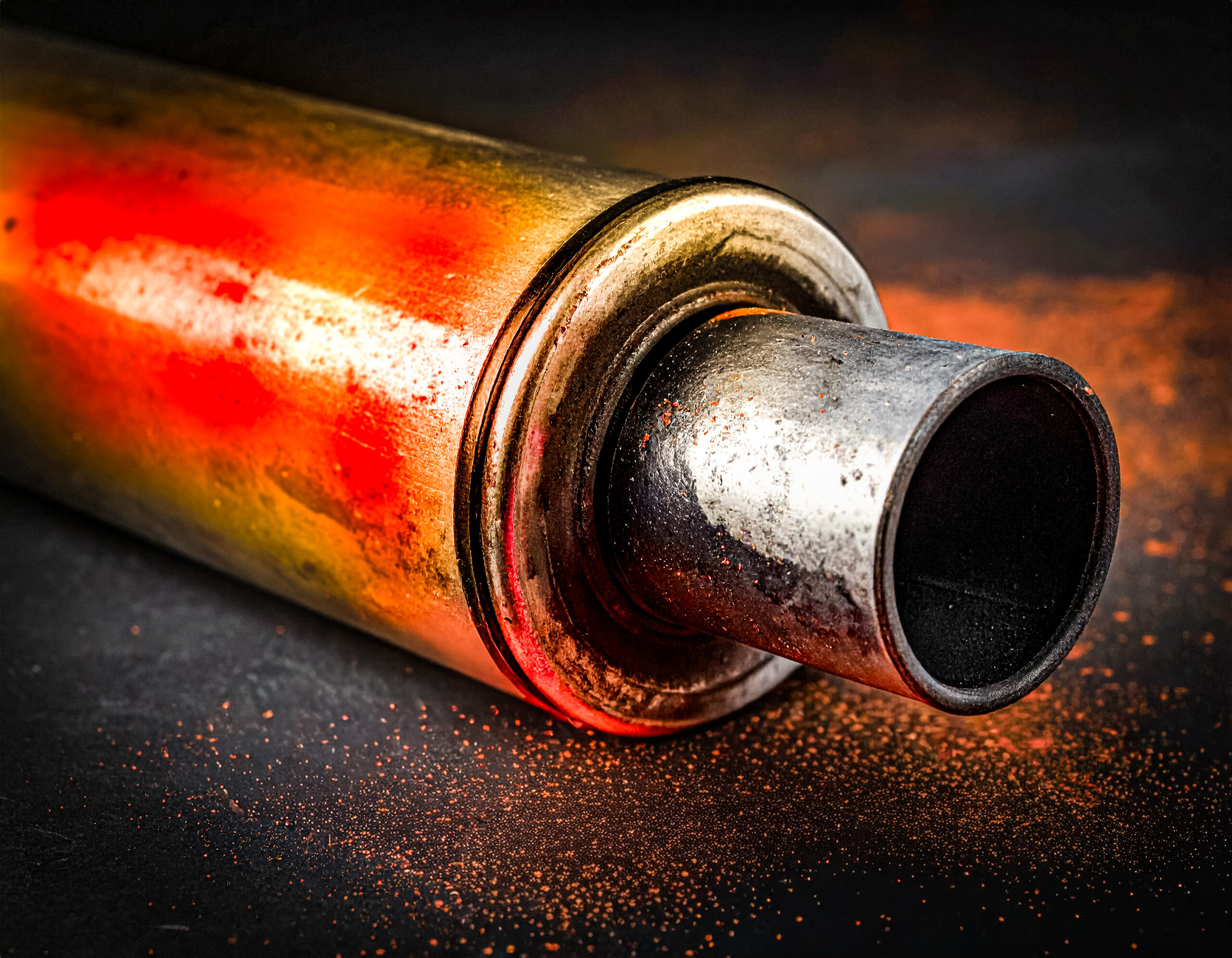 Abstract closeup of a catalytic converter spray painted with bright orange paint isolated on a dark background. Automotive design element.