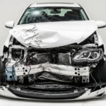 Damaged white car with crumpled hood and broken bumper