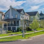 Panorama Whispy white clouds Row of large two-storey houses near the paved uphill road at Daybreak, Utah. View of houses from the intersection road with grass and trees near the sidewalk against the sky and mountains.