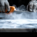 Gloved hands polishing marble slab with power tool, dust cloud, dark background, countertop use