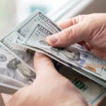 Financial transactions with cash money. Hands counting a stack of hundred-dollar bills.