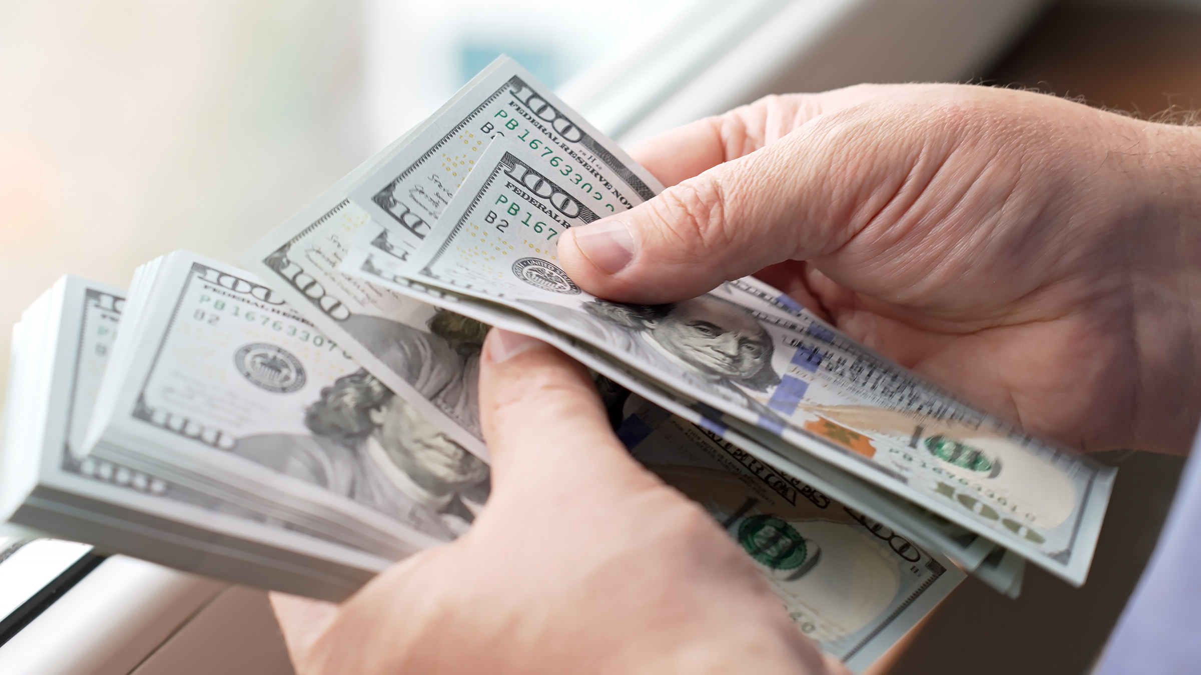 Financial transactions with cash money. Hands counting a stack of hundred-dollar bills.