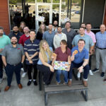 G&G Insurance employees gather for a group photo outside their office, some holding boxes of doughnuts