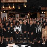 Mackoul Risk Solutions employees, many in 1920s-style costumes, pose for a group photo at an indoor murder mystery lunch