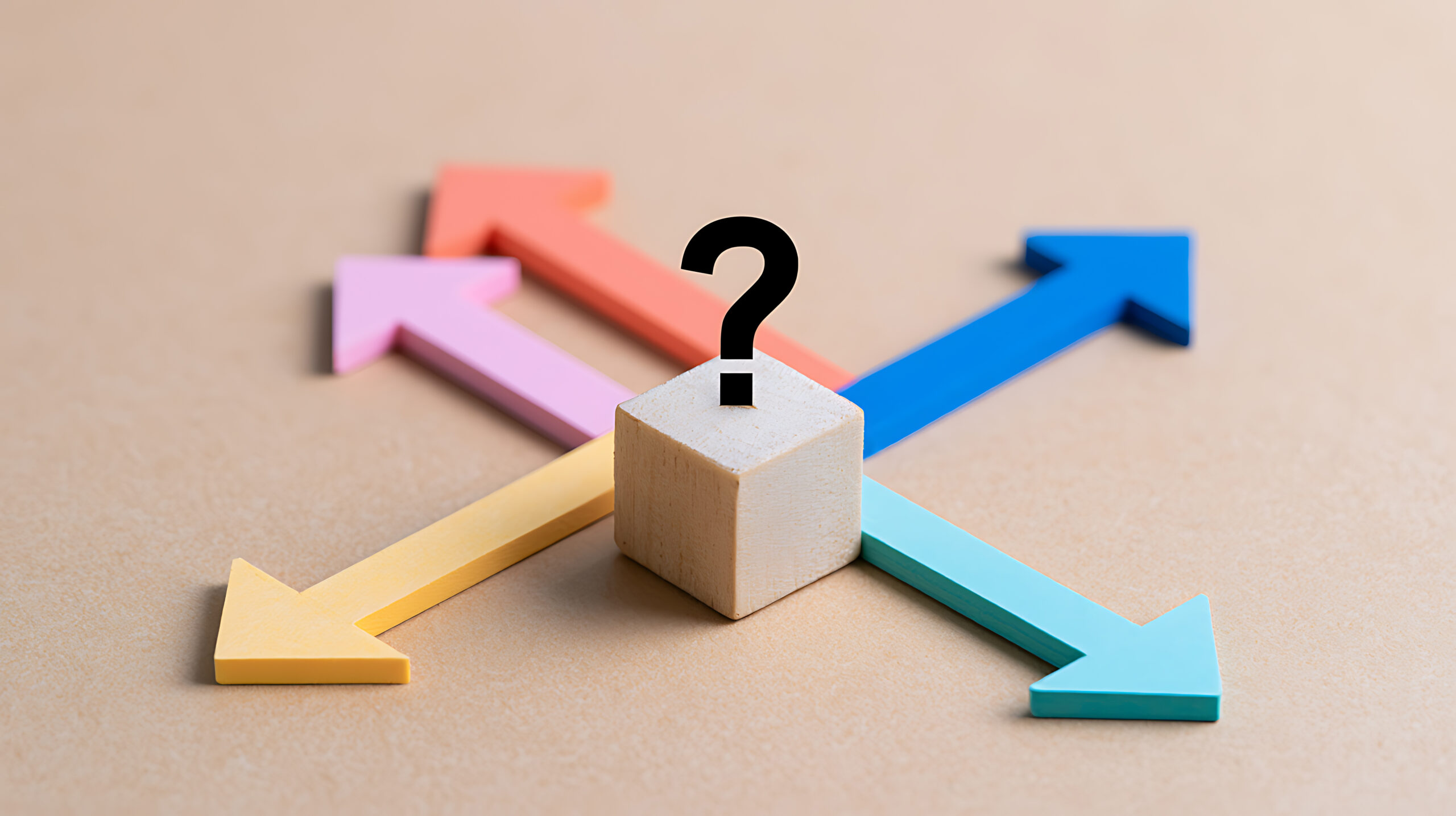 A wooden block with a question mark at a crossroads of colorful arrows pointing in different directions