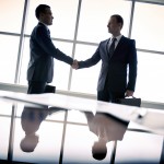 Silhouettes of two businessmen standing by the window and handsh